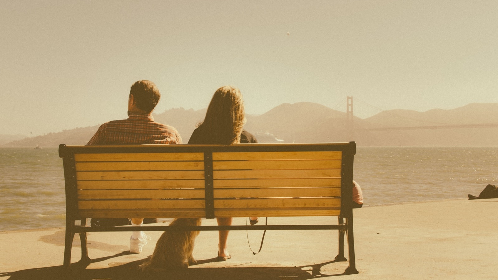 man and woman sitting on bench beside body of water